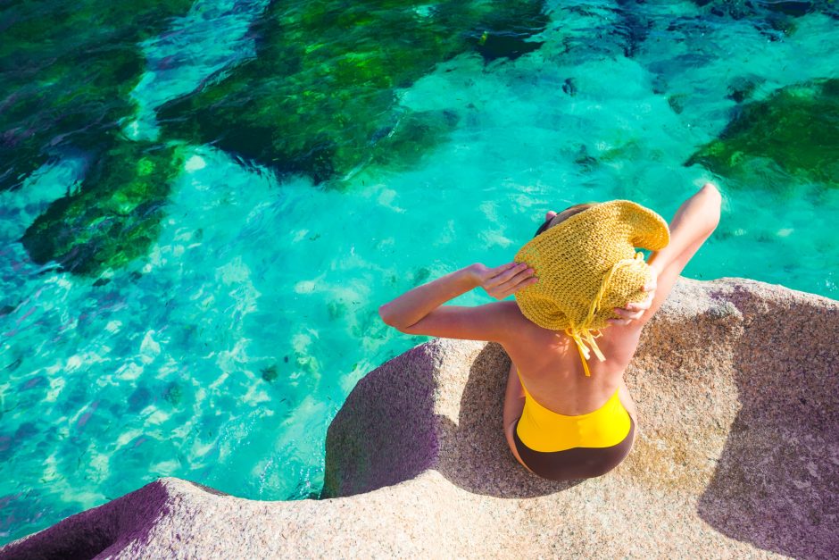 Woman in sun hat and swimsuit relaxing on the rocks over the sea Seychelles