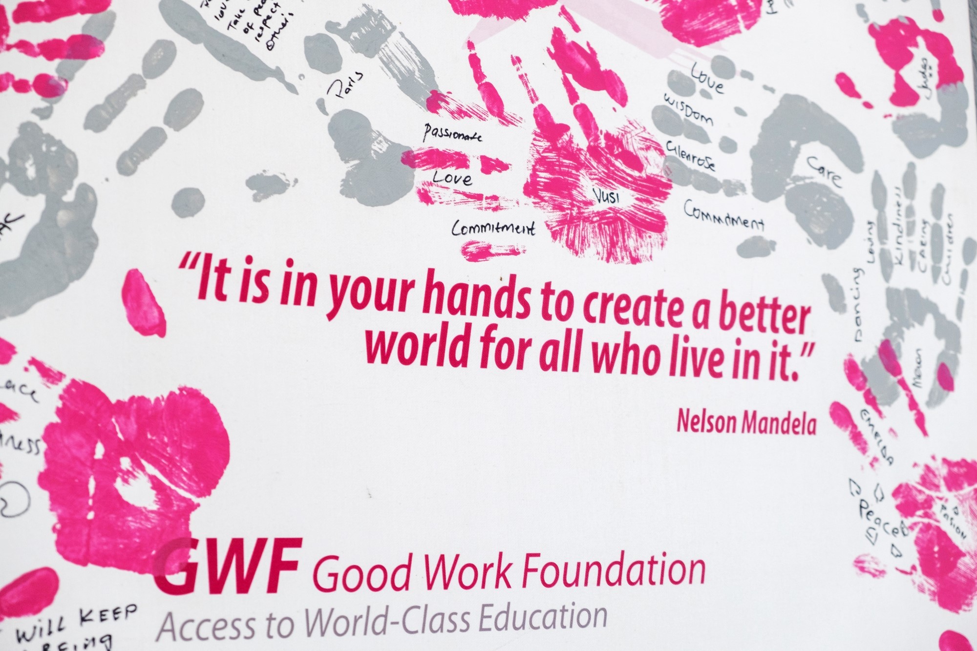 Felix-Studios-GWF-Aug-2022-152 A powerful quote by Nelson Mandela is displayed on a wall, surrounded by vibrant pink and grey handprints, some of which have words of inspiration written within them.