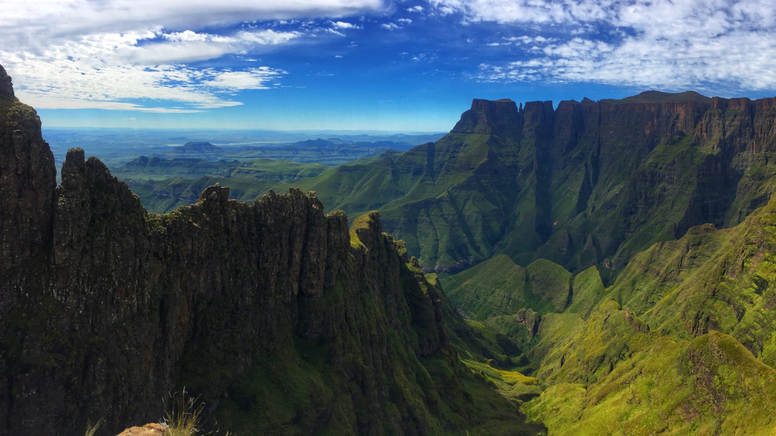 drakensberg-mountains-hiking-trail-south-africa-edit-229354479 The sun highlights the towering cliffs of the Drakensberg Mountains, casting light over the rugged peaks and lush valleys below.